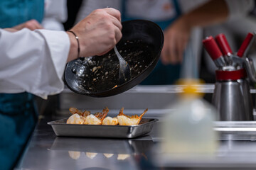 Mains d’un chef en train de faire cuire des langoustines dans une poêle chaude en cuisine professionnelle.