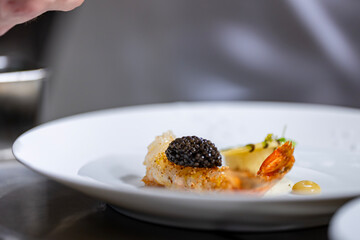Plat gastronomique en cuisine signé par un chef étoilé, mettant en scène une langoustine surmontée de caviar de Madagascar.