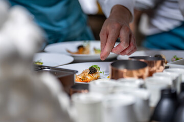 Main d’un chef étoilé en pleine préparation culinaire, dressant un plat gastronomique avec précision.