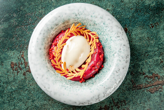 Gourmet dessert with berry mousse, white sorbet quenelle, golden tuile garnish, and red crumble, served on a ceramic plate. Artistic fine dining presentation