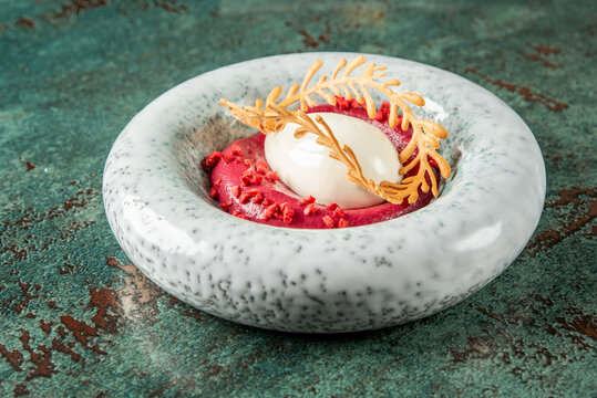 Gourmet dessert with berry mousse, white sorbet quenelle, golden tuile garnish, and red crumble, served on a ceramic plate. Artistic fine dining presentation