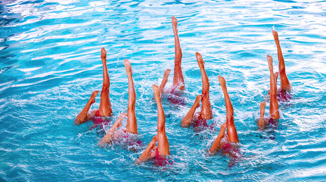 Group of athletes performing synchronized swimming routine in clear blue pool water during bright daylight