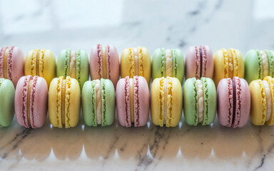 Colorful macarons on marble table. Row of assorted pastel-colored macarons placed neatly on a marble surface, highlighting sweetness and elegance — ideal for bakery and dessert themes.