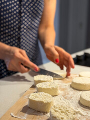 Woman in a dotted dress cutting cheese rounds on a wooden board in the kitchen