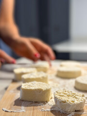 Woman preparing biscuits and arranging cottage cheese dough circles on a wooden board