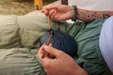 Woman playing steel tongue drum outdoors, relaxing meditation music instrument.