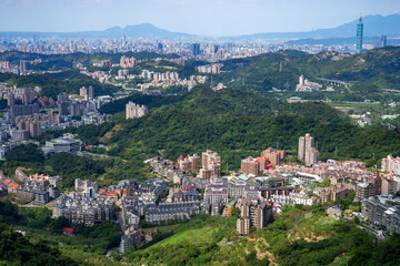 Panoramic view of Taipei city from an elevated perspective, showing dense urban development intertwined with lush green mountains and the iconic Taipei 101 tower in the distance, urban landscape.