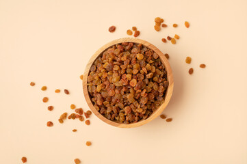 Sweet brown golden raisins in wooden bowl on beige background flat lay top view. Dried grapes berries. Food background. Ingredient for cooking, baking desserts