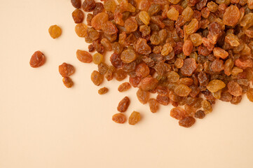 Dried golden brown raisins scattered on beige background flat lay top view. Grapes berries, sweet healthy snack, organic dried fruits. Food background, space for text