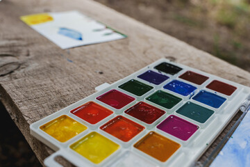 Young child painting with watercolor paints outdoors, creative activity in nature.