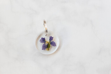 Handmade Clear Resin Keychain with Viola Odorata Flower on White Marble Background