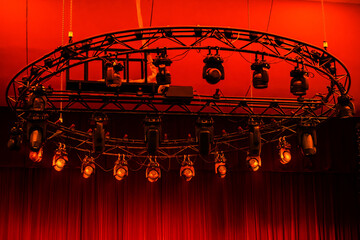 large round suspended structure with lighting equipment in a theatrical setting with a bright red curtain.