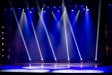 Empty theater stage illuminated with blue lighting and multiple spotlights. The scene creates an...