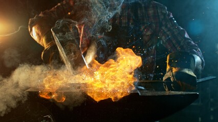 The blacksmith manually forging the molten metal on the anvil in smithy with spark fireworks