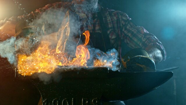 The blacksmith manually forging the molten metal on the anvil in smithy with spark fireworks - Powered by Adobe
