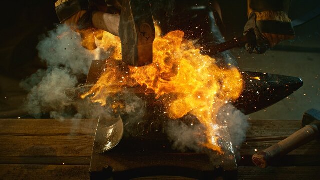 The blacksmith manually forging the molten metal on the anvil in smithy with spark fireworks - Powered by Adobe