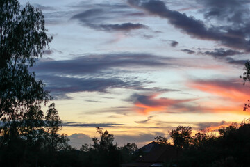 A breathtaking time lapse captures the sun's descent, casting a dramatic orange glow across storm clouds as they gather over the tree landscape