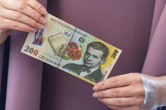 A hand holding a single Romanian 200 Lei banknote with a portrait of a famous writer.