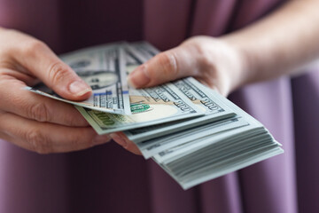 A person's hands holding and counting a stack of one hundred dollar bills.