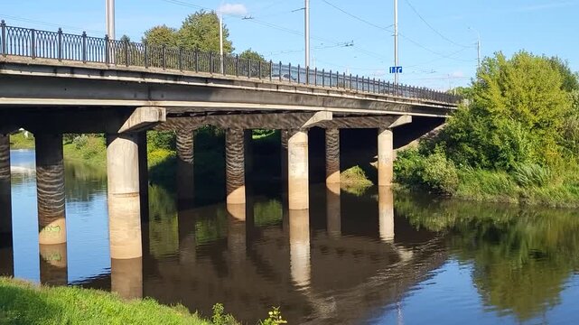 A car and pedestrian bridge over a small river with reflections on a sunny, bright summer day