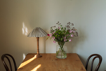 vintage table lamp and vase with summer flowers on a wooden table, warm light of the setting Sun,...