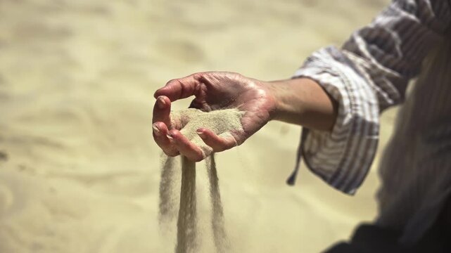 An extreme close-up of a woman's hand as dry sand slips through her fingers and scatters in the wind - a powerful slow motion visualization of land desertification