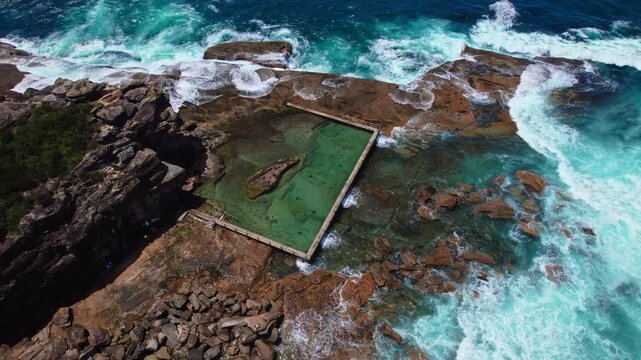 A stunning rock pool nestled in the rugged cliffs of an Australian beach, surrounded by crashing ocean waves under bright summer sunlight.