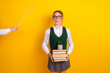 Cheerful schoolgirl holding books and wearing a classic uniform in front of a vibrant yellow...