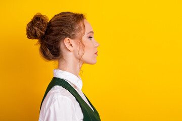 Side view portrait of young red-haired woman in stylish uniform standing against vibrant yellow...