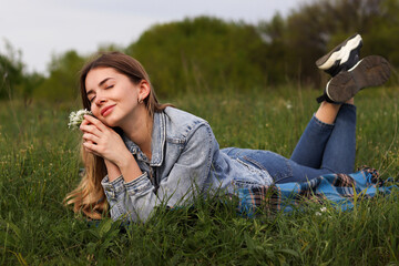 Girl with long hair sitting in nature and smiling. Beautiful young woman in a field with flowers.