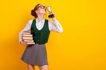 Young female student celebrating academic achievement while holding books and trophy against...
