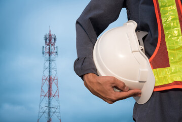 Communication engineer holding a white hard hat against a blue sky background