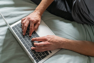 Man are sitting on a bed and working on laptop. Concept of online work or study