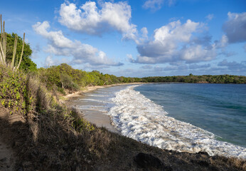 Waves crash onto sandy shore while the sun begins to set in the distance.