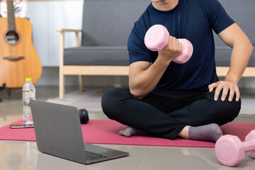 Home Fitness. Young man lifting dumbbell while watching workout video.