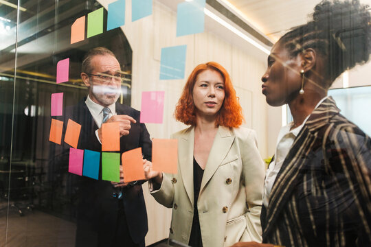 Diverse team collaborates in modern office, brainstorming with sticky notes on glass wall. Startup workshop highlights strategy, planning, leadership, teamwork, and creative meeting energy.