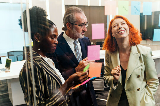 Diverse team collaborates in modern office, brainstorming with sticky notes on glass wall. Startup workshop highlights strategy, planning, leadership, teamwork, and creative meeting energy.