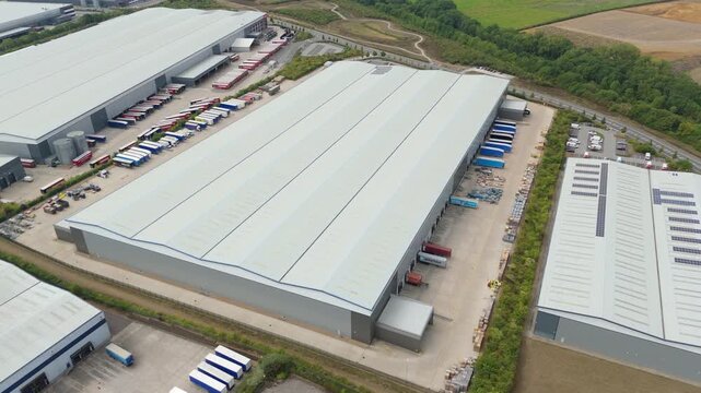 Aerial drone view of large industrial distribution centres, warehouses and factories, with heavy goods truck and trailers loading and unloading, Wellingborough England UK