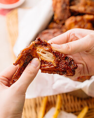 Close-up of hands tearing crispy fried chicken wing, showing juicy meat inside.