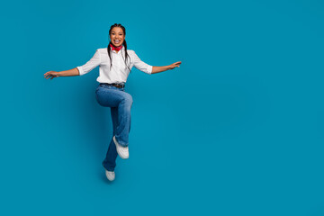 Obraz premium A cheerful young woman posed against a blue background wearing casual fashion and displaying joyful energy