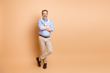 Confident mature businessman in casual formalwear posing with arms crossed against a beige...