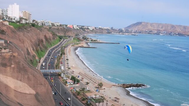 Paraglider flying over the miraflores district coastline, lima, peru, with the morro solar in the background