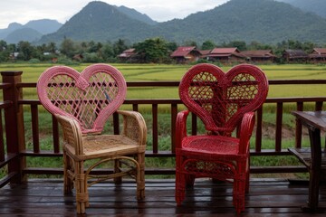 Heart-shaped wicker chairs on a wooden balcony overlooking a rice paddy landscape