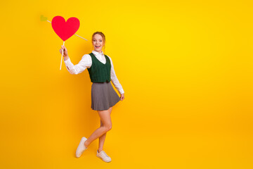 Cheerful young woman holding a heart sign and gesturing joyfully while posing against a vibrant...
