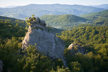 Beautiful panorama of mountain rock surrounded by green foliage with hills and slopes on background