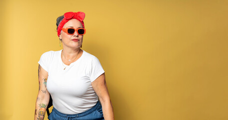 Stylish senior woman posing with sunglasses and headband on yellow background