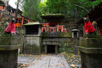 Stone fox guardians at Fushimi Inari Shrine in Kyoto, draped in red bibs, symbolize protection and...