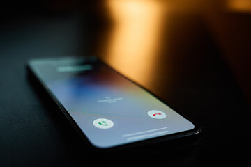 Close-up of smartphone lying on table in dark room with incoming call on screen. Concept of...