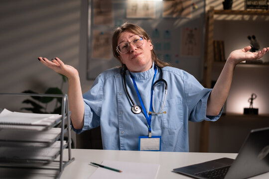 Confused nurse working overtime on night shift can't help, makes gesture of I dont know in hospital office. Difficult question. Health care and medicine service