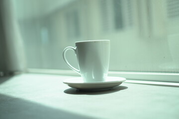 a white mug and coaster sitting near a window with the copy object right in the middle